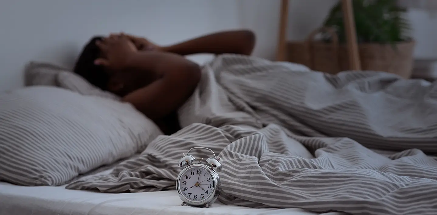 A person lying in bed, hands over face, struggling to fall asleep