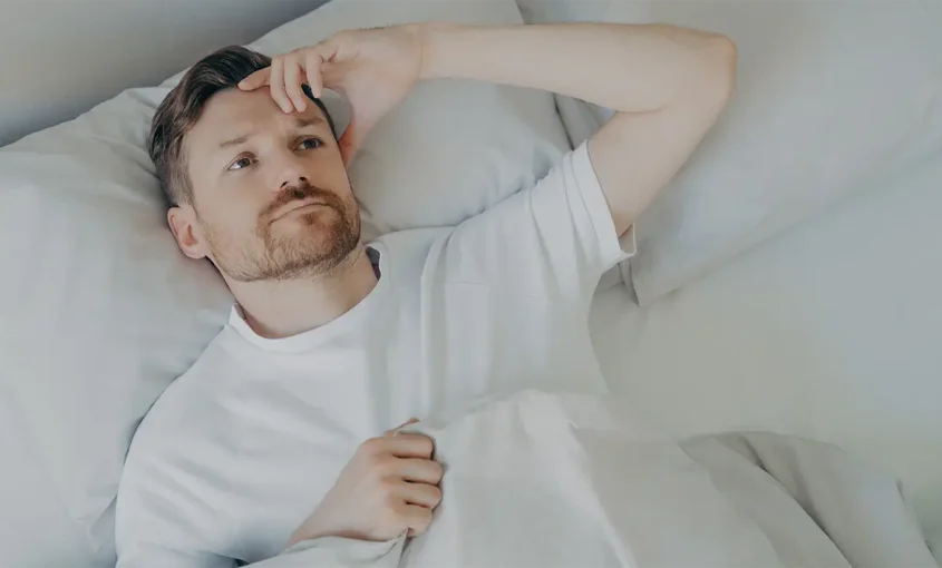 A man lying in bed, his head on a pillow, not being able to sleep because of sleep apnea.