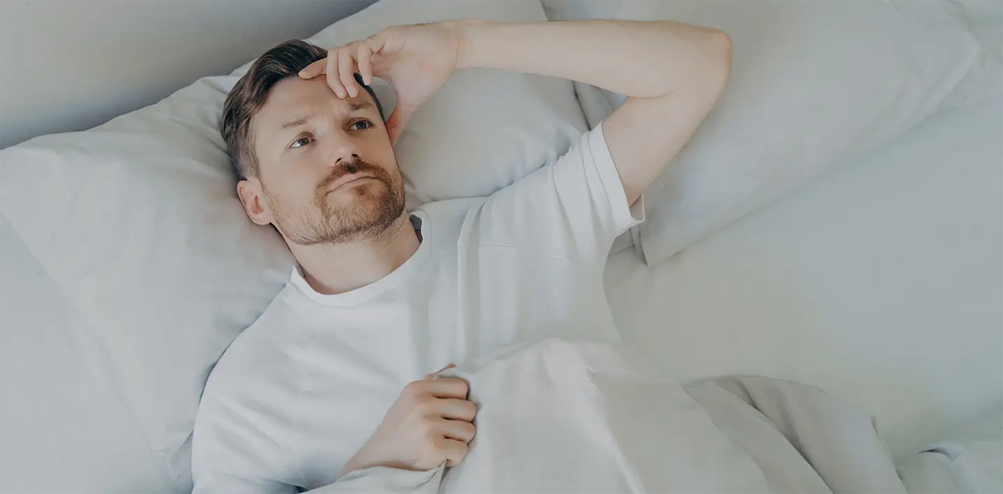 A man lying in bed, his head on a pillow, not being able to sleep because of sleep apnea.