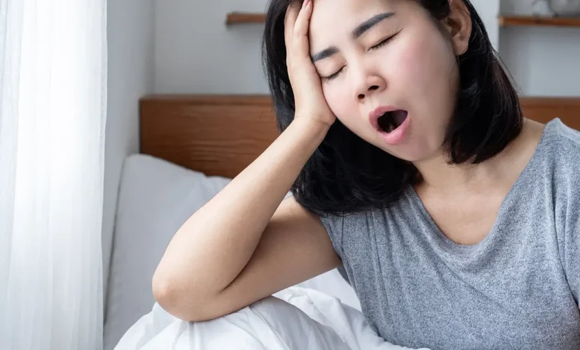 A woman sitting on a bed, yawning, conveying a sense of fatigue.