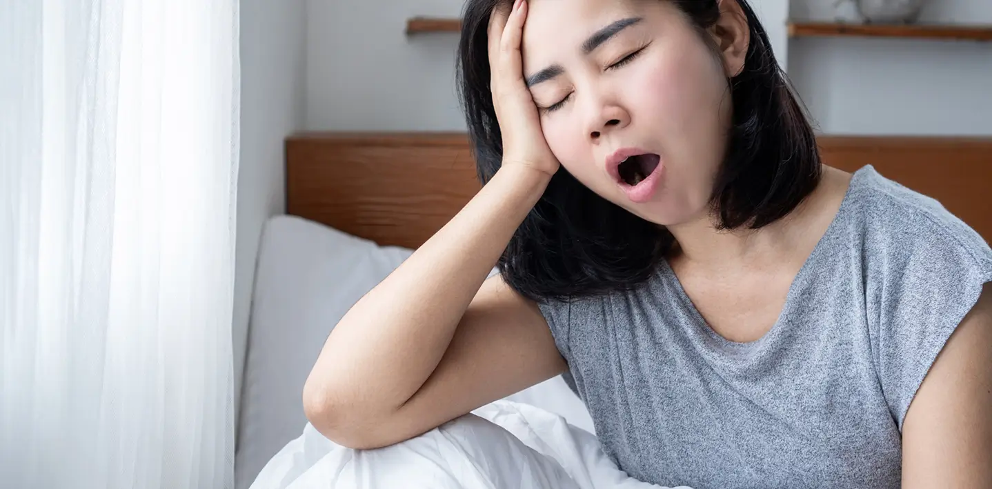 A woman sitting on a bed, yawning, conveying a sense of fatigue.